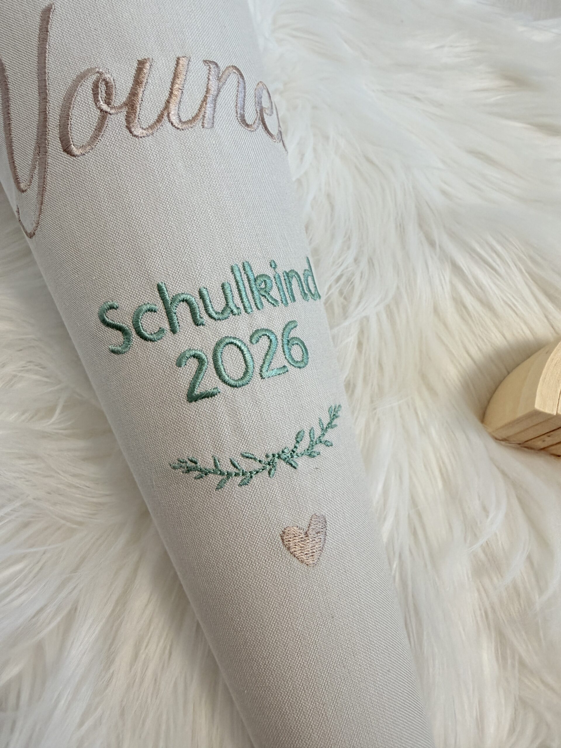Nahaufnahme der Stickerei Schulkind 2026 mit grünem Zweig und beigefarbenem Herz