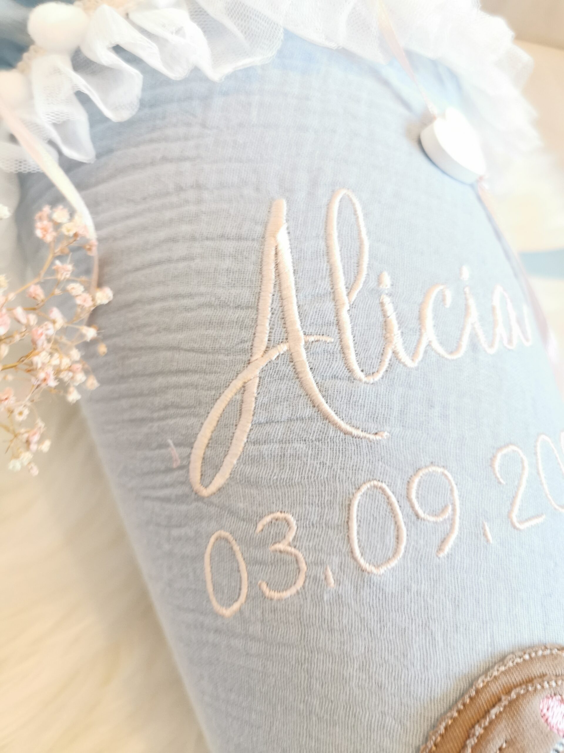 Nahaufnahme des aufgestickten Namens Alicia und des Datums auf hellblauem Musselin