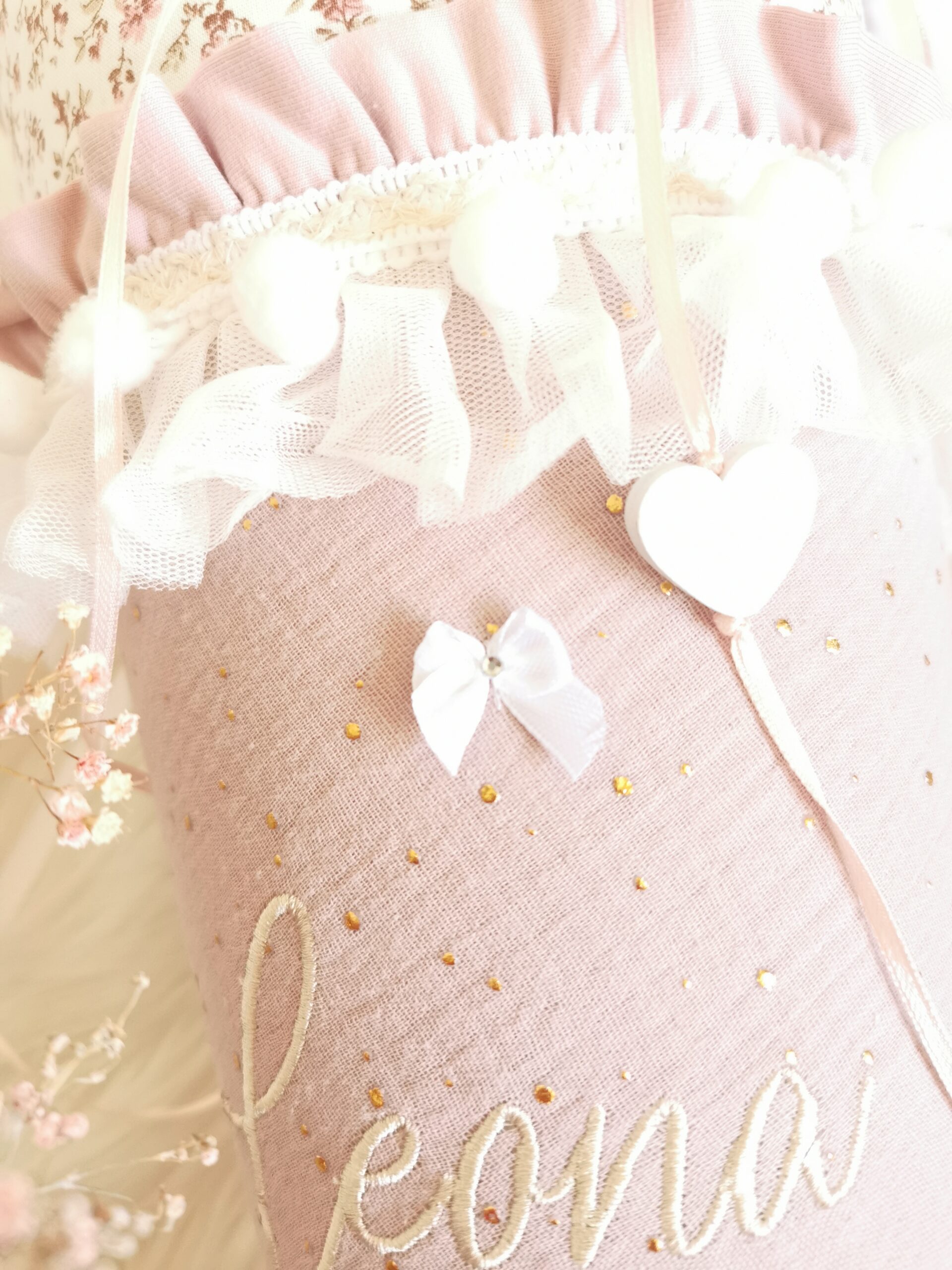 Nahaufnahme von Herzanhänger, weißer Schleife und goldenen Punkten auf rosa Musselin