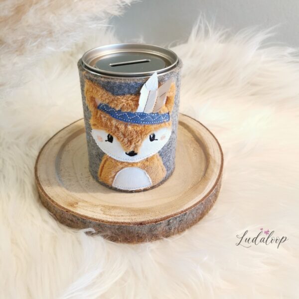 Graue Spardose mit Fuchsapplikation, blauem Stirnband und Stofffedern auf einer Holzscheibe