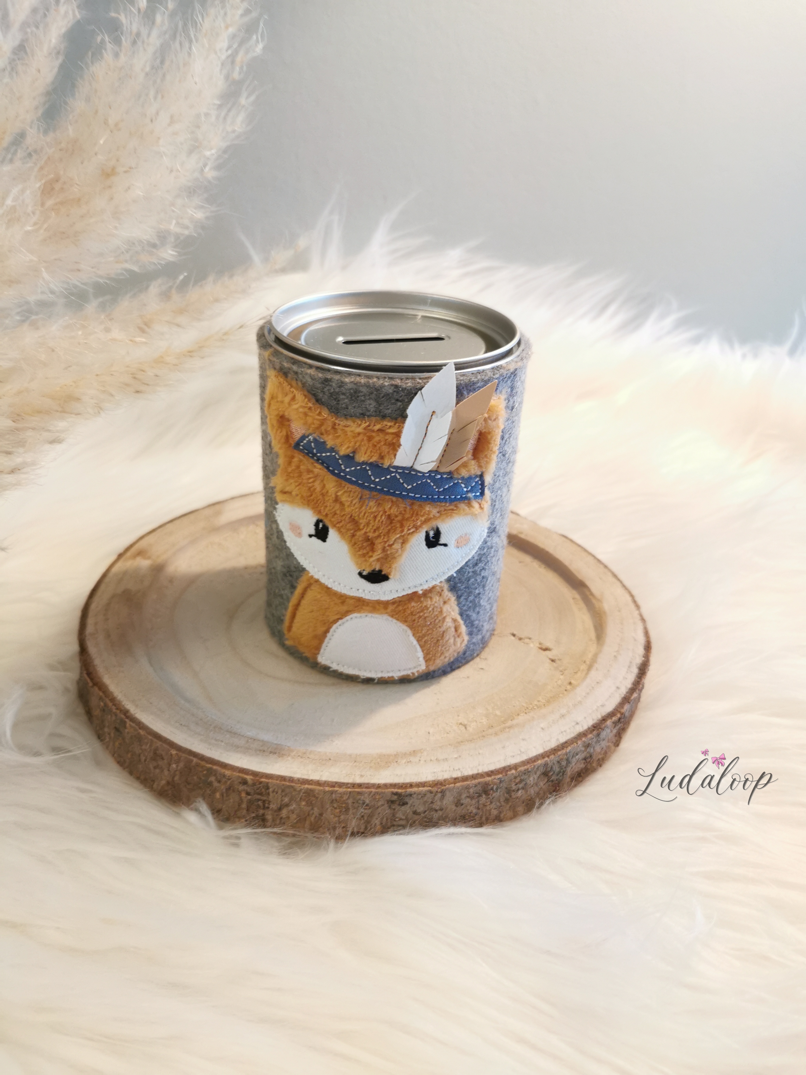 Fuchs-Spardose mit grauem Filzmantel und silbernem Deckel auf einer Holzscheibe